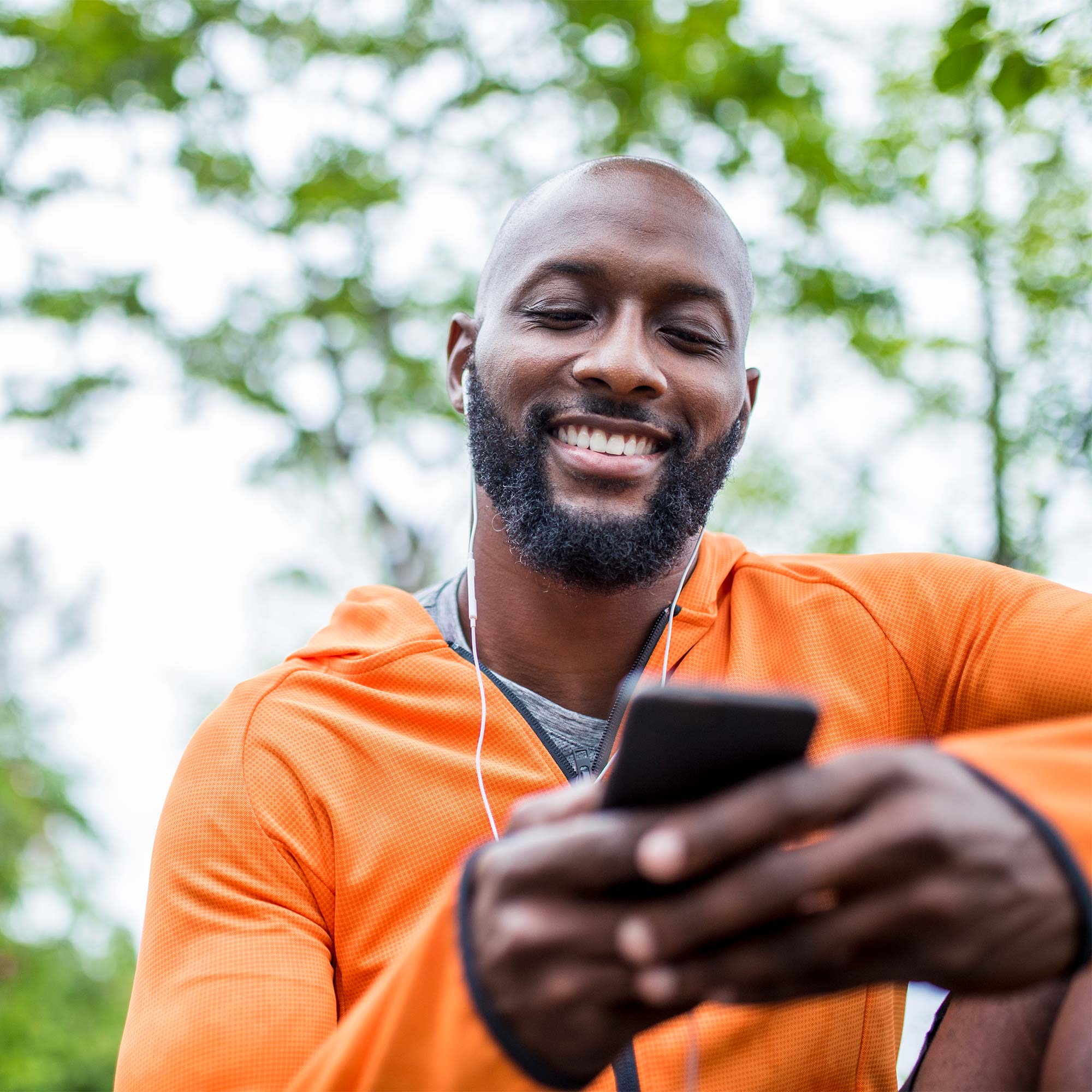 A man wearing an orange jacket smiling and looking at his phone.